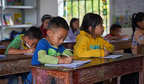 Ung elev skriver konsentrert notater i et klasserom